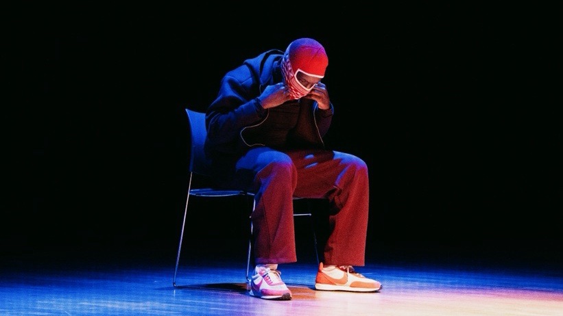 Solo performer seated on a stage under a spotlight